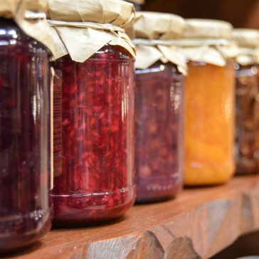 A close-up view of various homemade jam jars lined up on a wooden shelf.