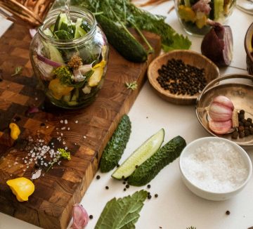 Top view of fresh ingredients for pickling cucumbers with herbs and spices on a wooden cutting board.